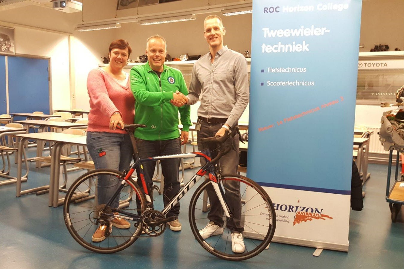 Sandy en Carl Dekker van Bike Shop Egmond overhandigen docent Jan Bosman een Scott Speedster racefiets. Foto Horizon College