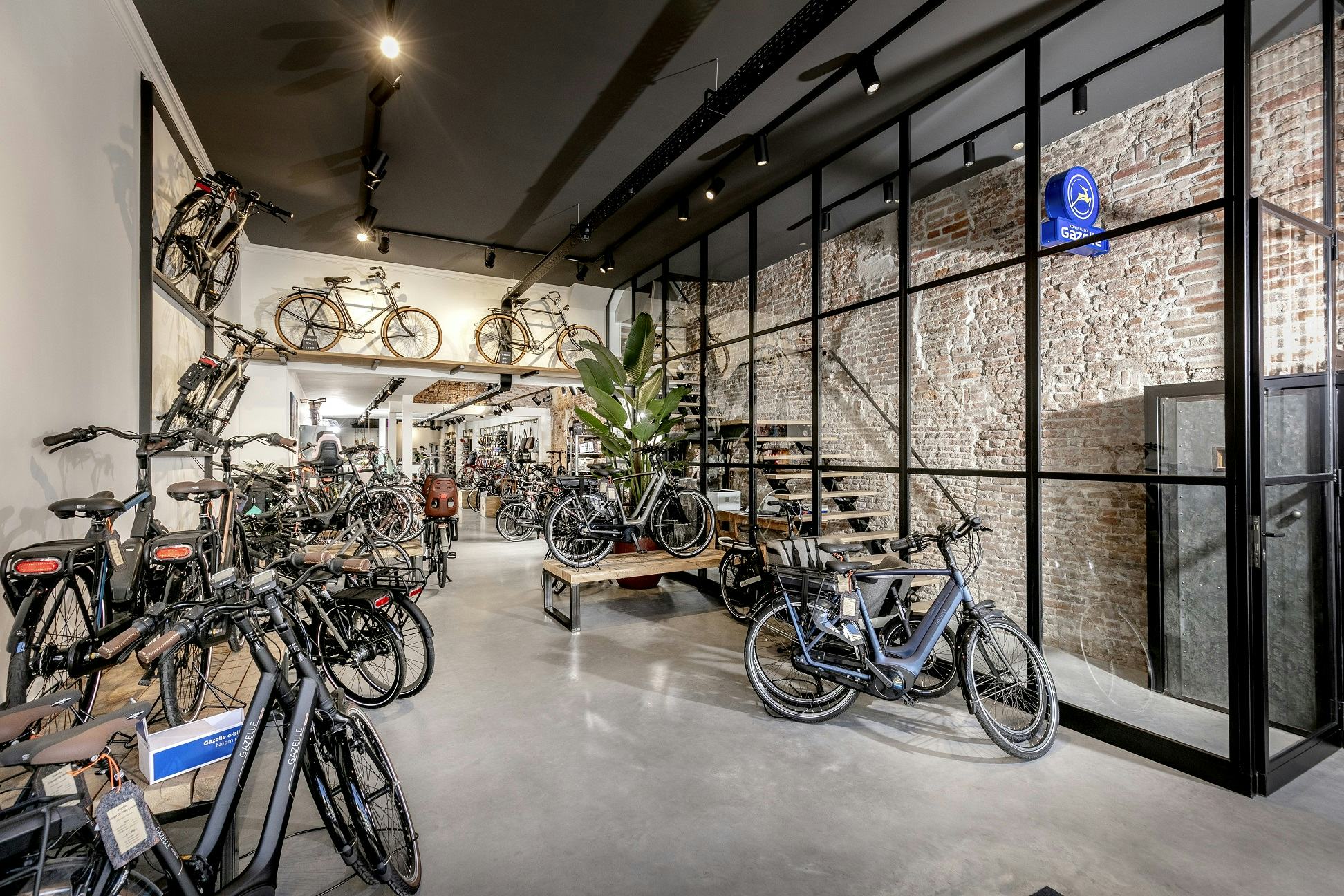 De winkel heeft een industriële uitstraling en alles is professioneel afgewerkt. De afscheiding tussen de winkel en de trap naar het woongedeelte bestaat uit een moderne glazen wand met zwarte kozijnen. Rechts zijn de oude gevangenisdeuren te zien die de meterkast afsluiten.