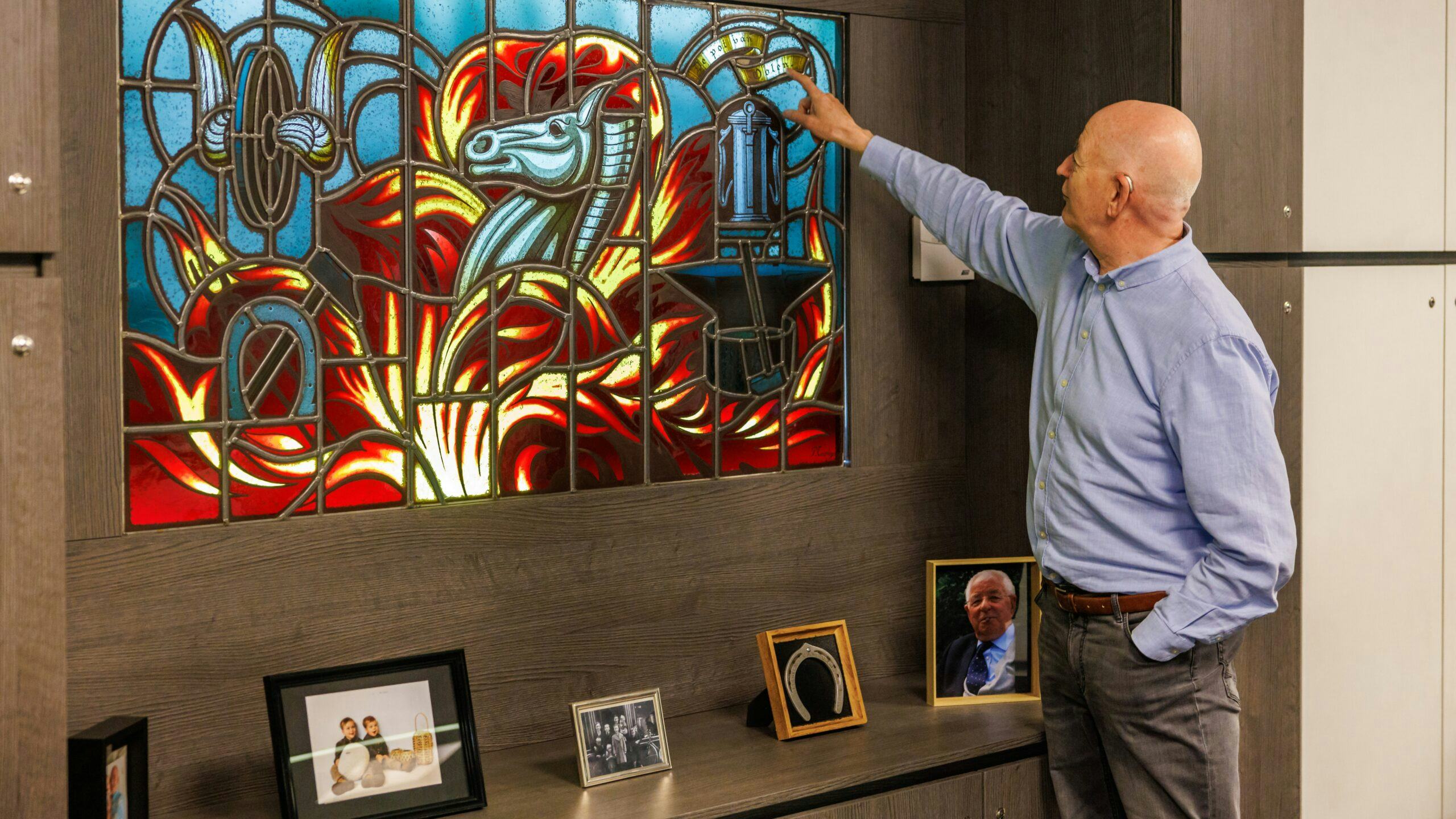 Eddy Van Hemelen laat het glas-in-loodraam zien dat op zijn kantoor hangt. Foto: Rhode Van Elsen
