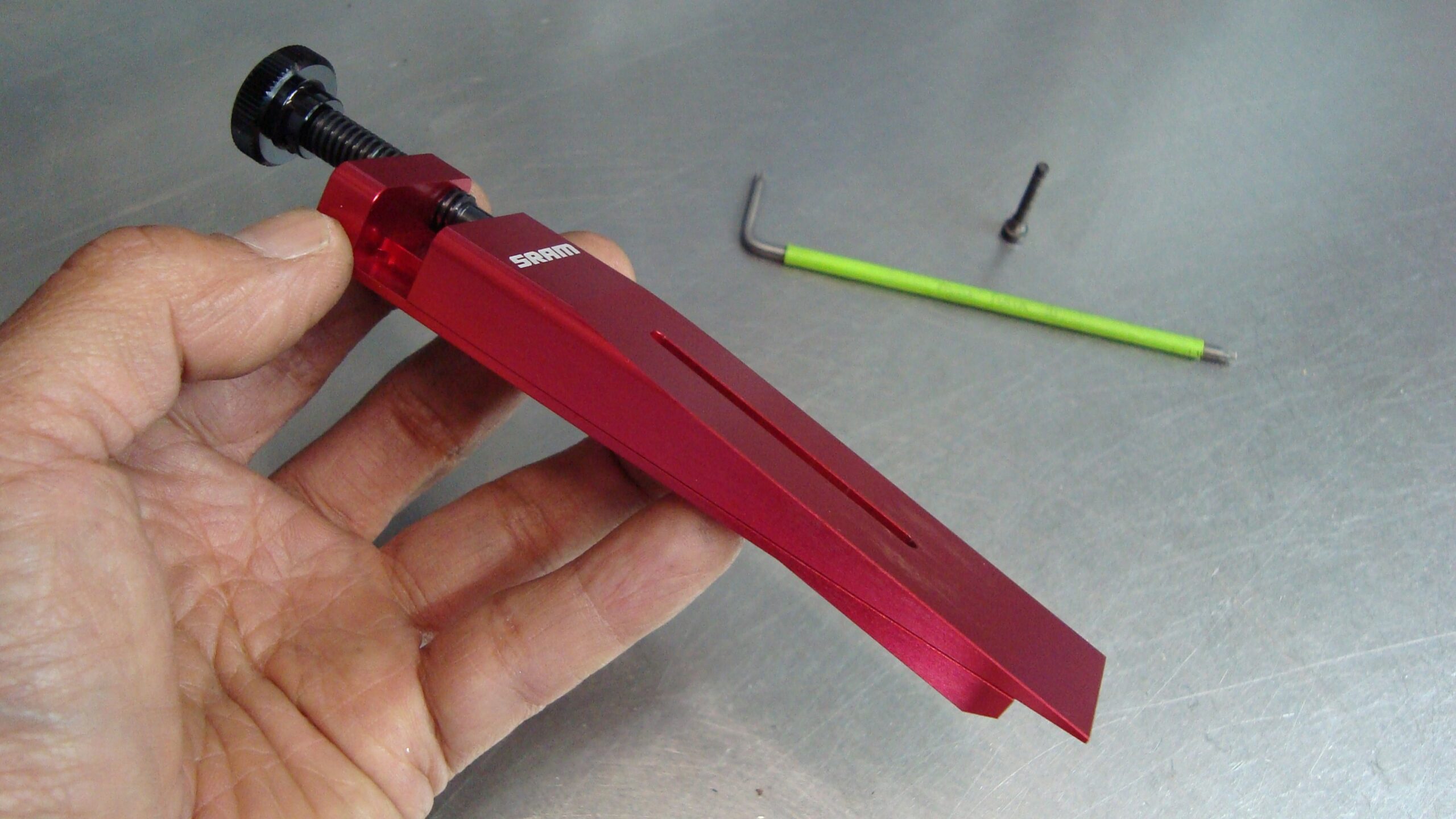 De SRAM ultimate piston spreader zet je vast met het remblok bevestigingboutje, waarna je door de wig constructie heel geleidelijk de zuigers terug kan drukken.